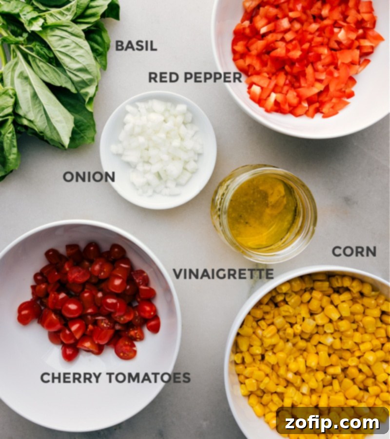 A flat lay shot displaying all the fresh ingredients for the Tomato and Corn Salad, including corn kernels, cherry tomatoes, bell pepper, onion, and basil.