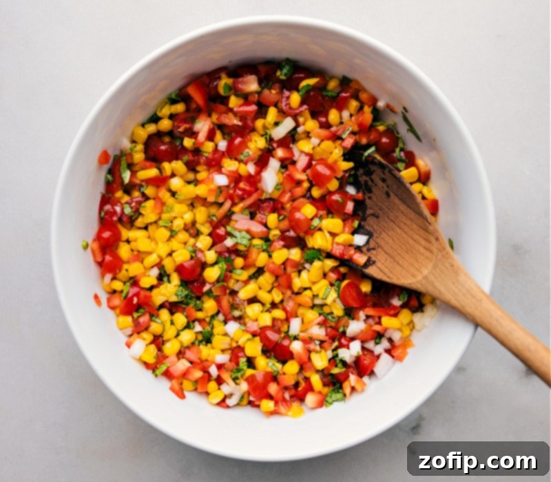 Overhead view of a beautifully prepared bowl of Corn and Tomato Salad, with a wooden serving spoon resting within, ready to be enjoyed.