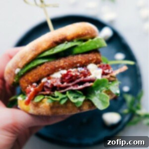 An appetizing close-up of the English Muffin Sandwich ingredients, layered and ready to be enjoyed, including a crispy hash brown, bacon, avocado, pesto, and feta