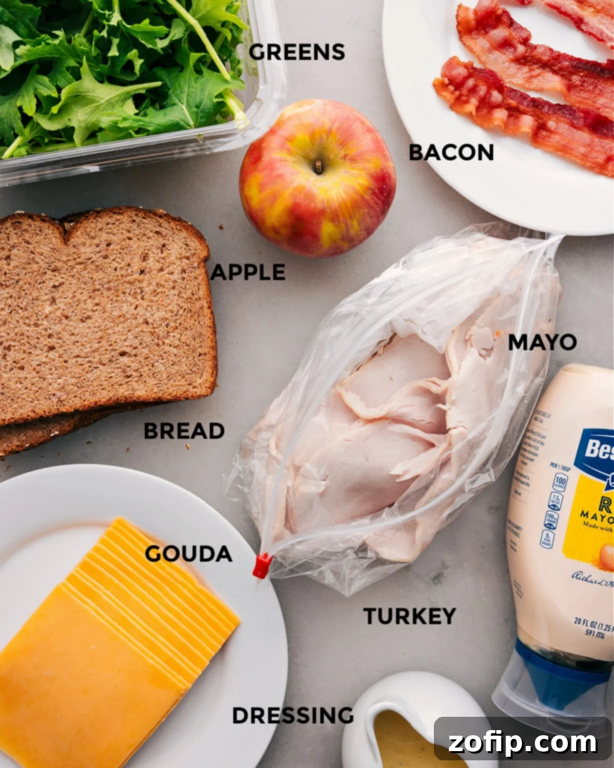All the fresh ingredients for this gourmet turkey sandwich, including sliced meats, crisp apple, fresh greens, toasted bread, creamy cheese, mayo, and a vibrant dressing, are meticulously prepped for seamless assembly.