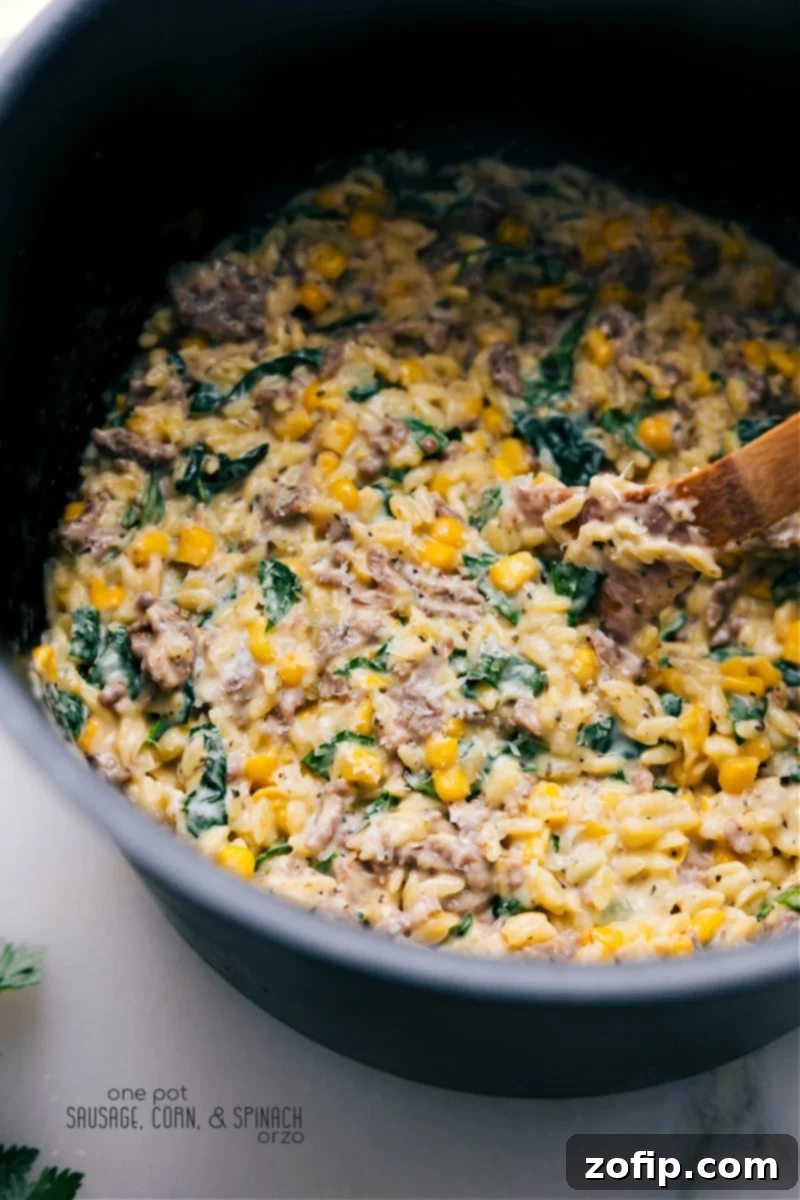 Overhead image of a large serving bowl filled with creamy Sausage, Corn, and Spinach Orzo, garnished with fresh parsley and extra Parmesan cheese.
