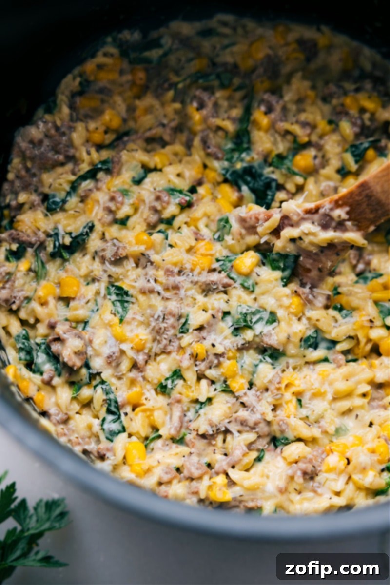 Up-close overhead image of a creamy Sausage, Corn, and Spinach Orzo dish in a large pot, ready to be scooped and enjoyed, garnished with fresh herbs.