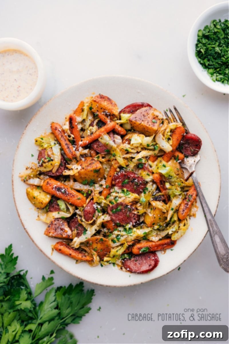 One-Pan Cabbage, Potatoes, and Sausage combines smoky sausage with roasted veggies, topped with Parmesan and a creamy Dijon sauce – a hearty, flavorful, and easy weeknight dinner. Overhead shot of the finished One-Pan Cabbage, Potatoes, and Sausage dish, perfectly roasted and drizzled with sauce.
