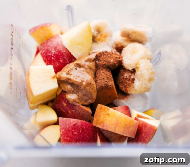 Gathering fresh ingredients to blend a wholesome Apple Pie Protein Smoothie. Fresh apples, warming spices, and creamy almond butter being added to a blender for the smoothie.