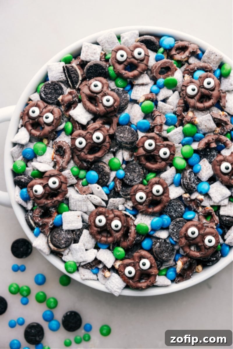 Close-up view of Goblin Goodies snack mix, highlighting the texture of the coated cereal, mini Oreos, M&M's, and the cute pretzel goblins with edible eyes.