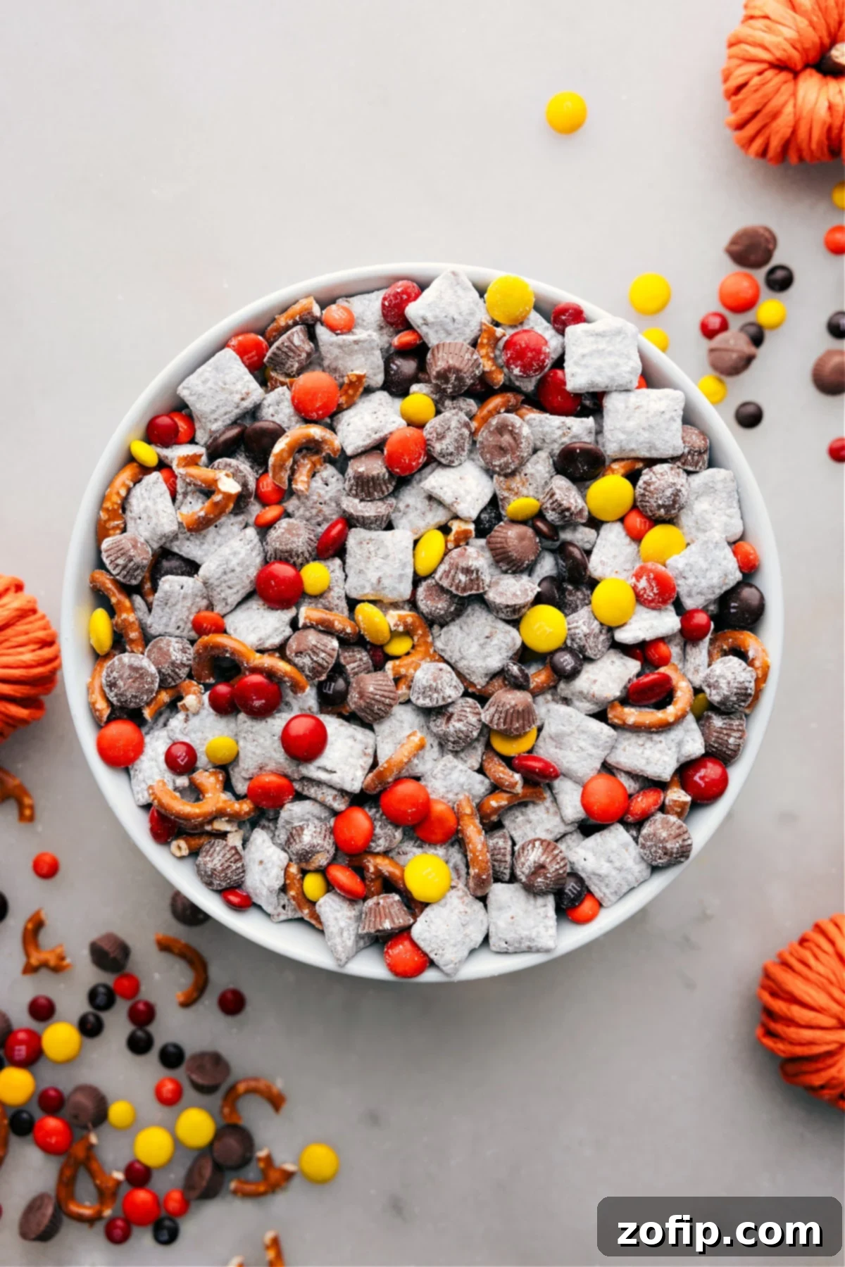 A vibrant bowl of Fall Muddy Buddies, showcasing crispy Chex cereal coated in rich chocolate and powdered sugar, studded with colorful autumn candies and salty pretzel pieces, ready to be enjoyed.