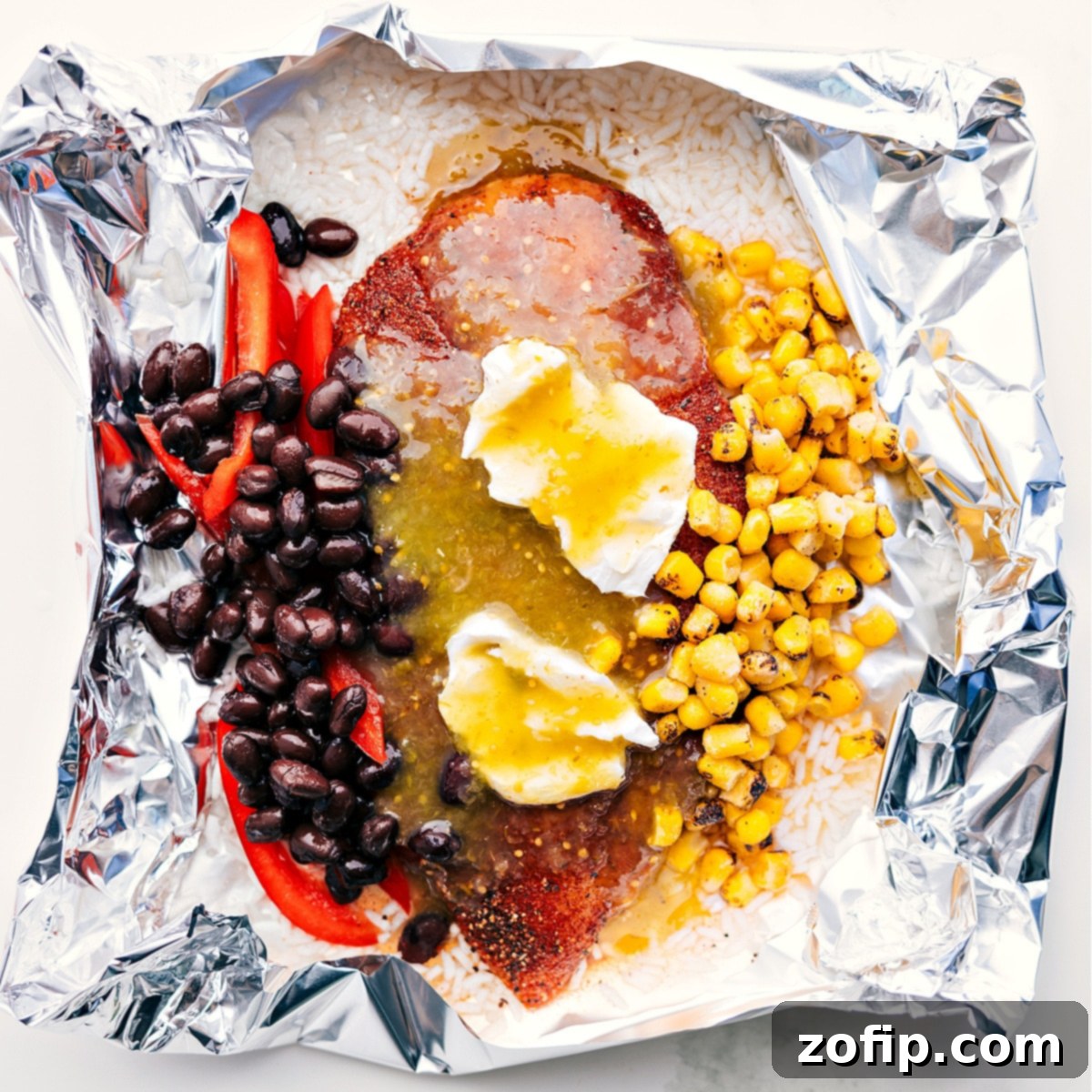 Foil packet filled with rice, corn, beans, cream cheese, salsa verde, and chicken, ready to be cooked over a fire, grill, or in the oven.