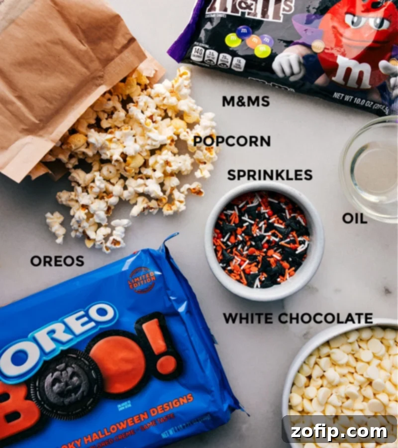 Ingredient shot: All the items needed for Halloween Popcorn, including popcorn, Halloween Oreos, Halloween M&M's, white chocolate chips, and vegetable oil