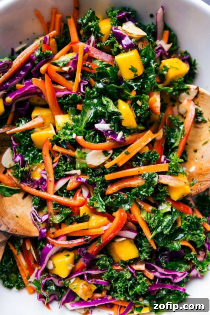 Colorful bowl of the completed kale salad recipe, complete with wooden serving spoons.
