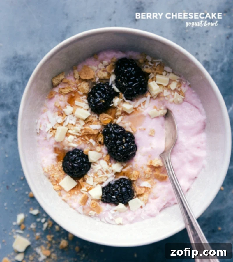 A vibrant Strawberry Cheesecake Yogurt Bowl, beautifully topped with fresh blackberries, crunchy graham cracker crumbs, and delicate chopped white chocolate, creating a dessert-like breakfast.