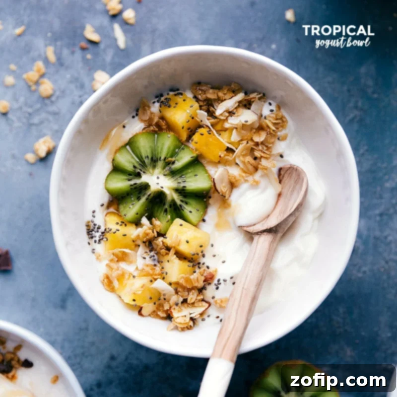 A delightful Tropical Yogurt Bowl featuring vibrant green kiwi slices, golden pineapple chunks, and a sprinkle of crunchy granola, ready to be enjoyed with a spoon.