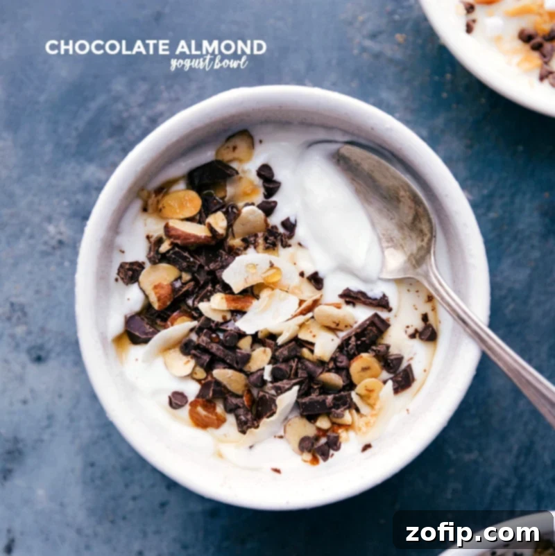 An indulgent Chocolate-Almond Yogurt Bowl featuring creamy yogurt adorned with chopped dark chocolate, mini chocolate chips, and honey-roasted sliced almonds, ready to be enjoyed with a spoon.