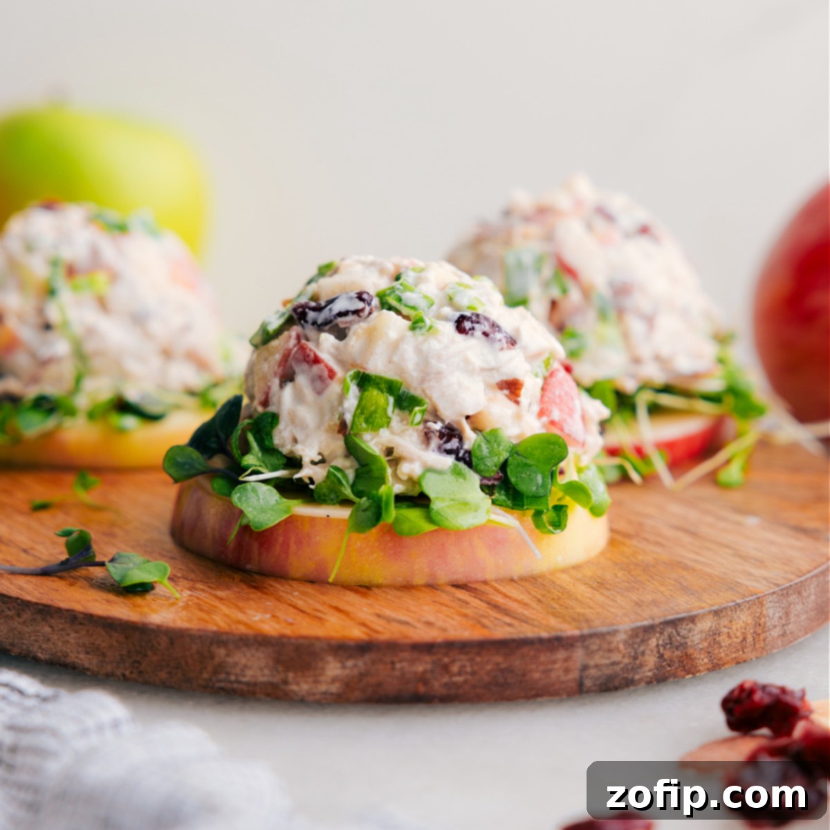 A serving of fresh chicken salad with apples, presented elegantly on a crisp apple slice, garnished with microgreens.