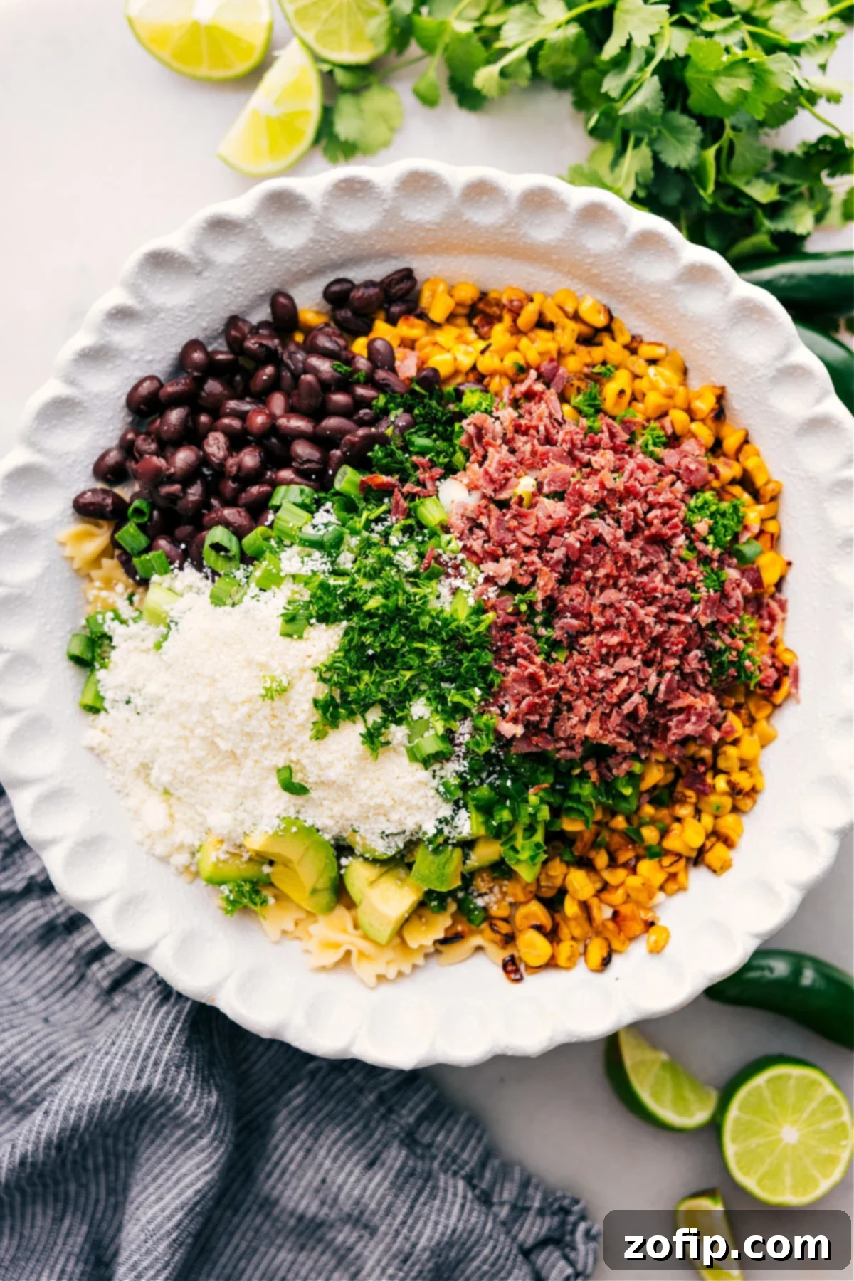 Assembling The Best Mexican Street Corn Pasta Salad A wide shot of a large mixing bowl filled with all the prepared ingredients for Mexican Street Corn Pasta Salad – perfectly cooked pasta, smoky charred corn, creamy diced avocado, tender black beans, vibrant cilantro, crisp green onions, savory bacon, and crumbled cotija cheese – waiting for the final drizzle of dressing.