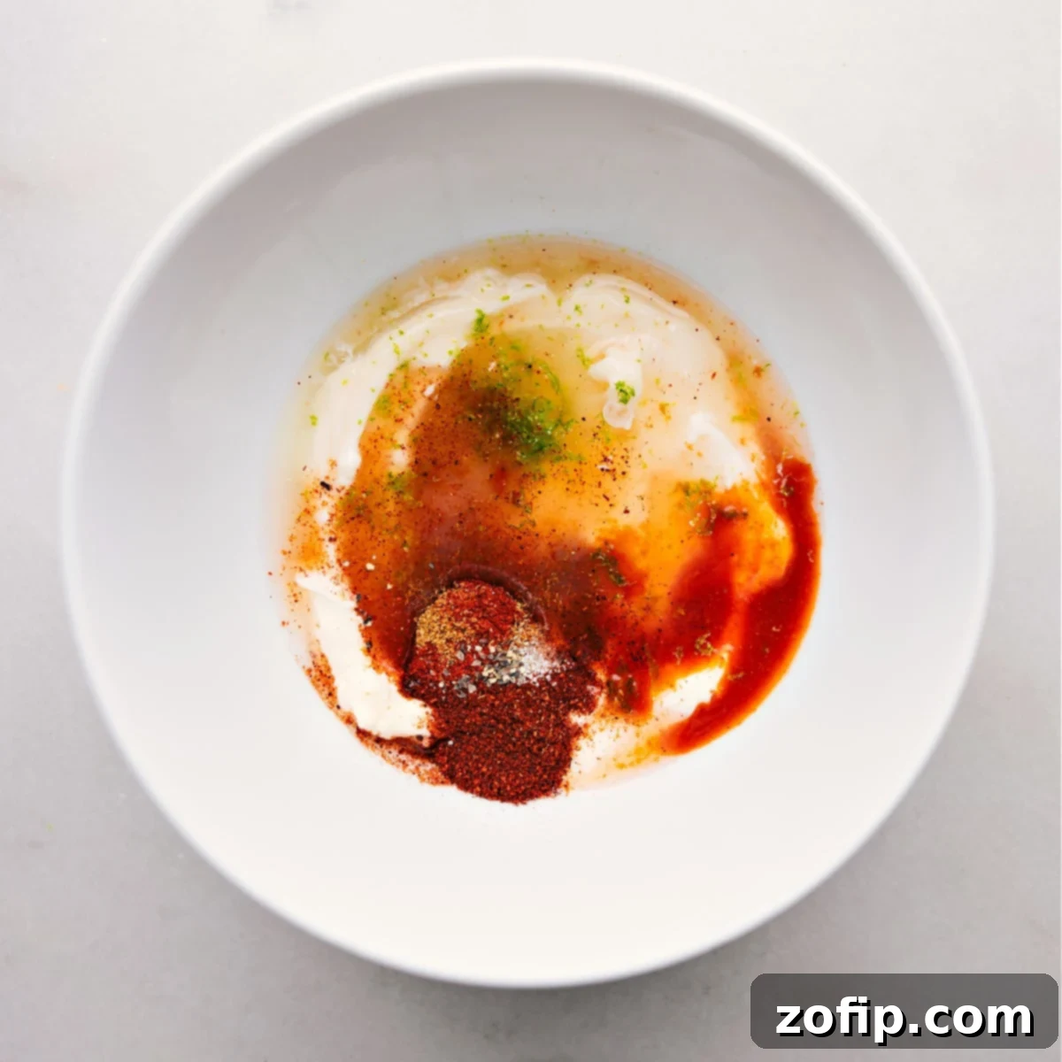 Ingredients for Fish Taco Sauce, including creamy condiments and spices, in a bowl ready for mixing.