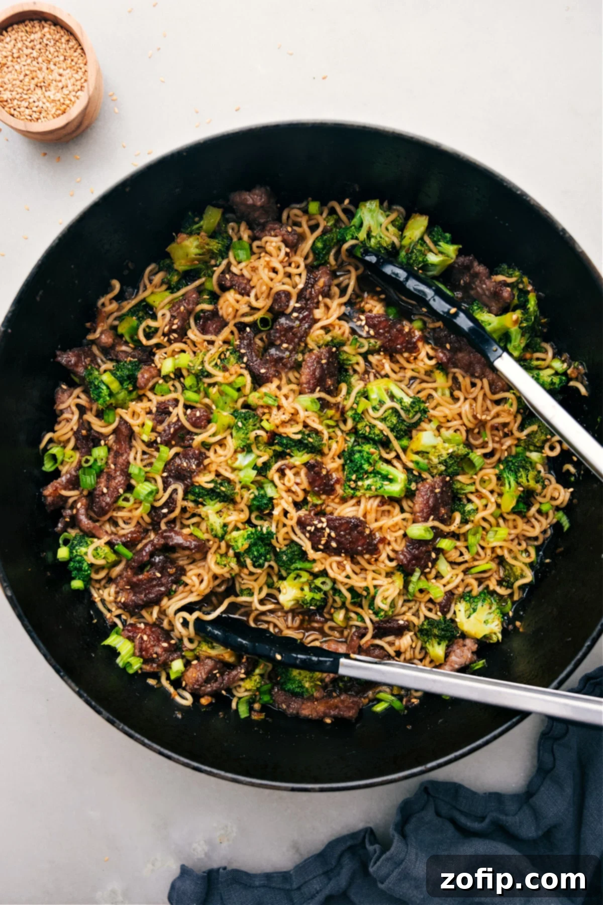 A vibrant pot of Beef and Broccoli Ramen, with serving tongs ready to dish out a delicious portion.