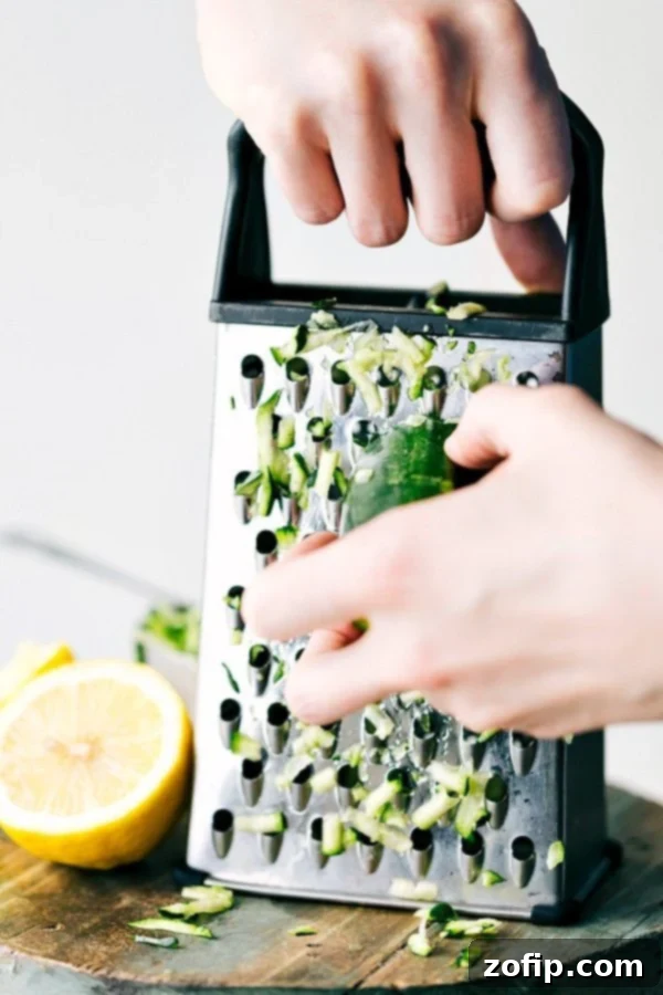 Shredding fresh zucchini on a box grater, a preparatory step for making delicious lemon zucchini bread.