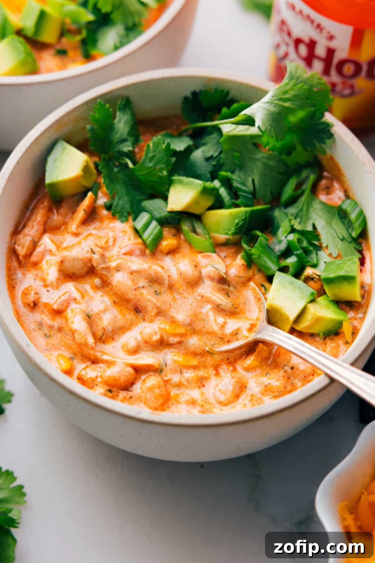 A big bowl of Buffalo Chicken Chili with a spoon in it, garnished with fresh toppings.