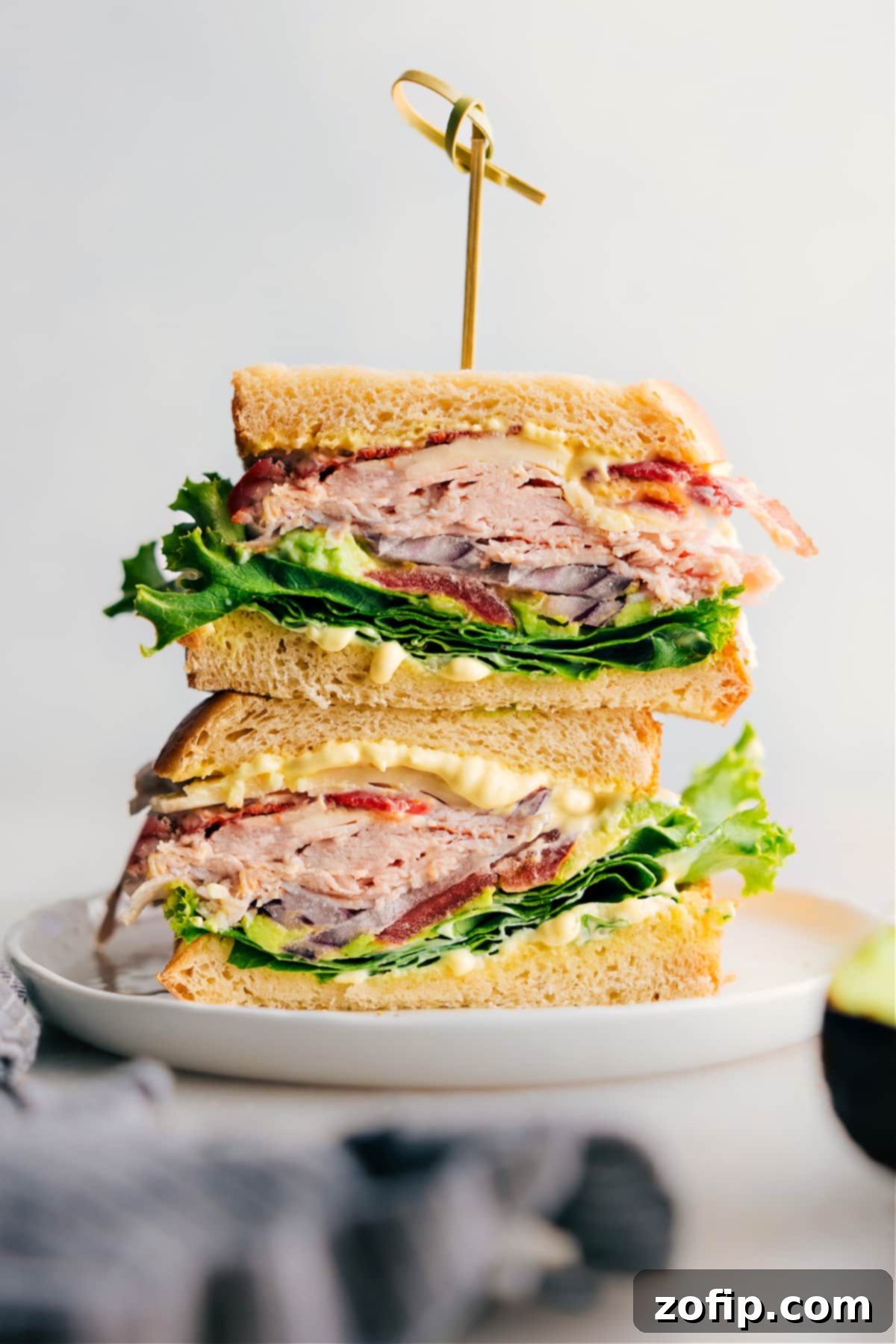A thick, flavor-packed Turkey Bacon Avocado Sandwich featuring Thanksgiving leftovers, fresh vegetables, and a savory homemade sauce, artfully arranged on a cutting board.