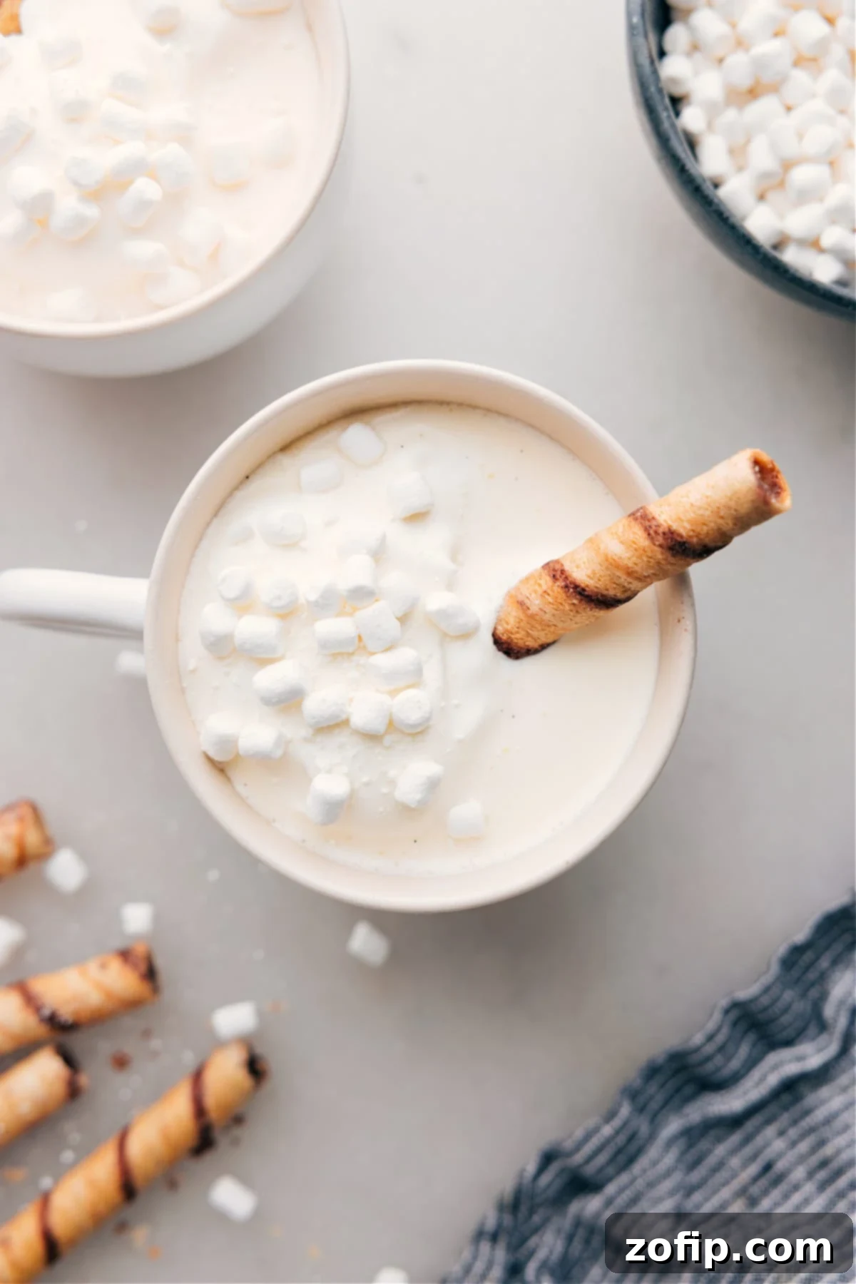 A mug of warm and delicious White Hot Chocolate, with marshmallows floating on top and a chocolate straw coming out of it.