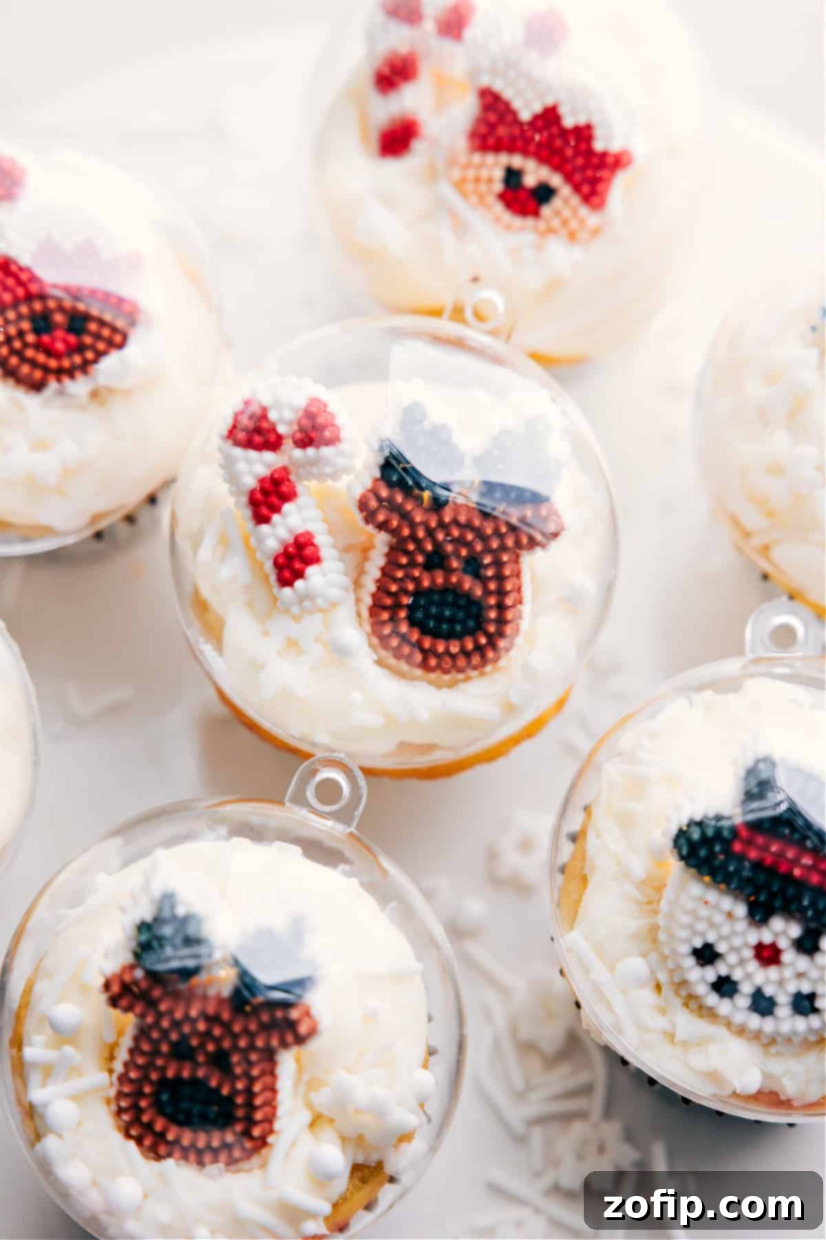 Closeup of Reindeer and Candy Cane Snow Globe Christmas Cupcakes A close-up view of two intricately designed festive Christmas cupcakes, one adorned with an adorable reindeer figurine under a clear snow globe dome and the other featuring miniature candy canes, highlighting the creative and whimsical holiday toppings.