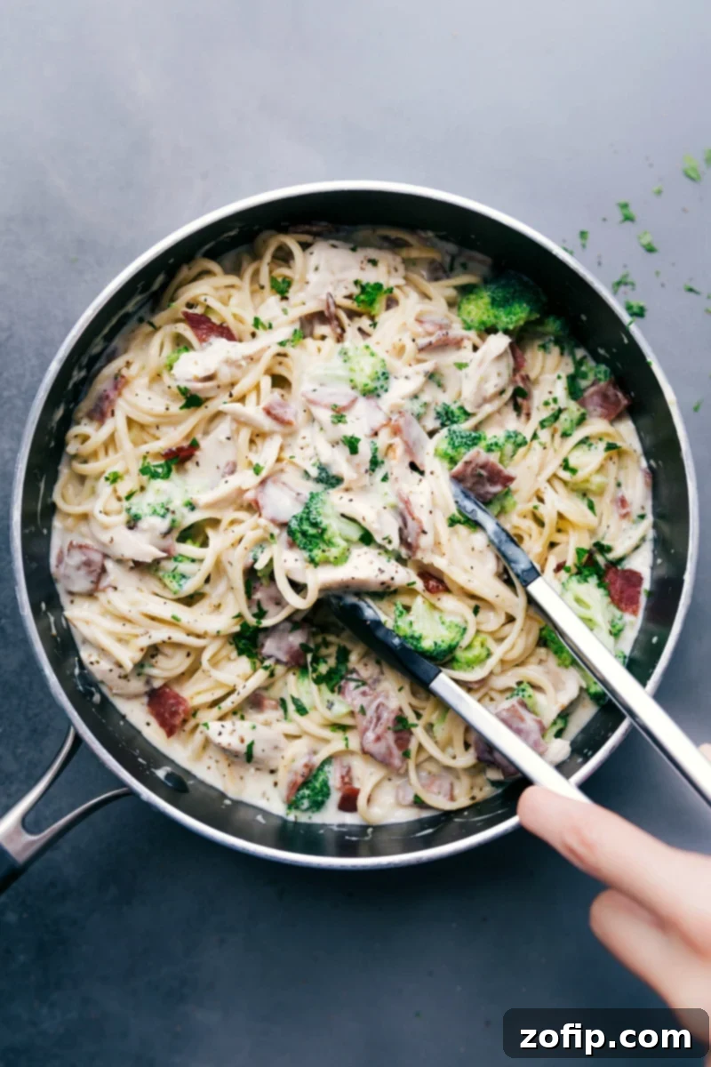 Chicken broccoli alfredo with tongs scooping up a creamy and delicious bite, ready to be enjoyed.
