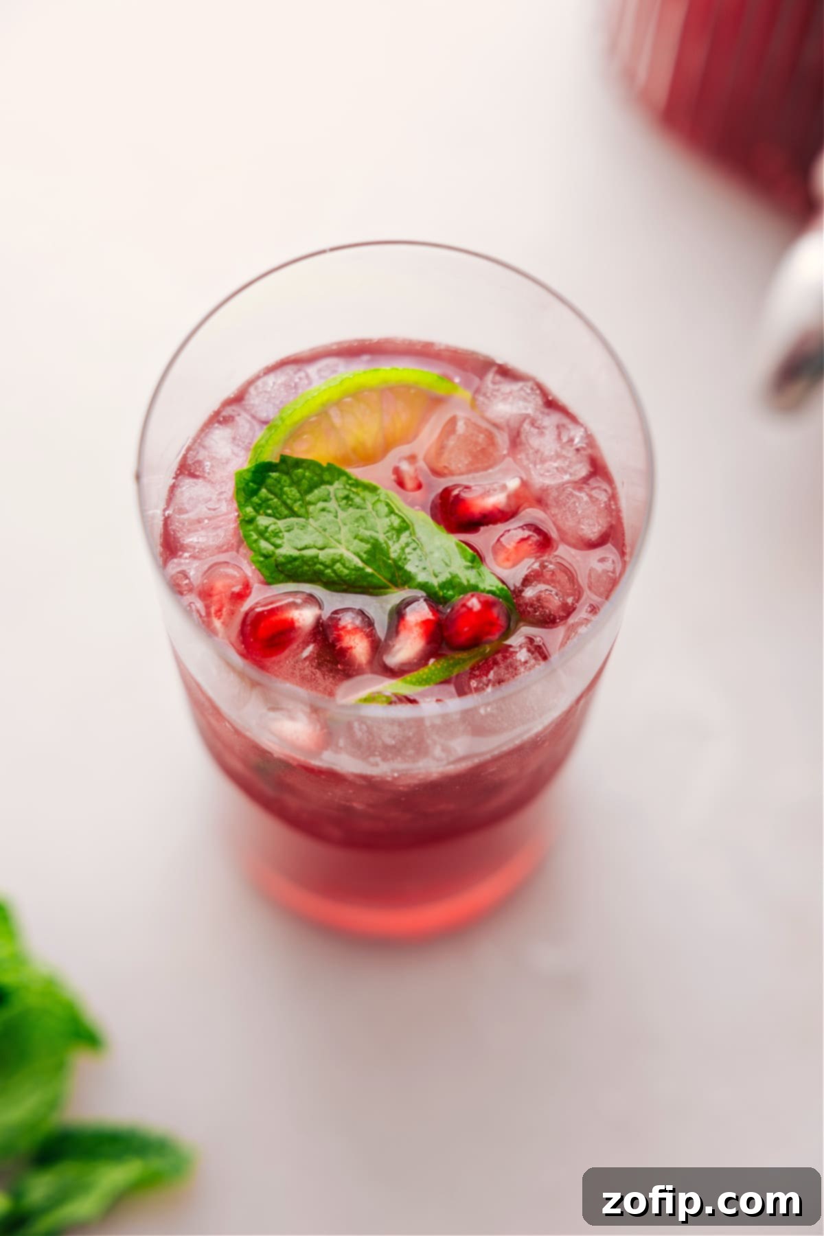 A close-up shot of a large glass punch bowl filled with vibrant Christmas Punch, adorned with numerous fresh mint sprigs and lime slices, emphasizing its rich flavor and appealing presentation.