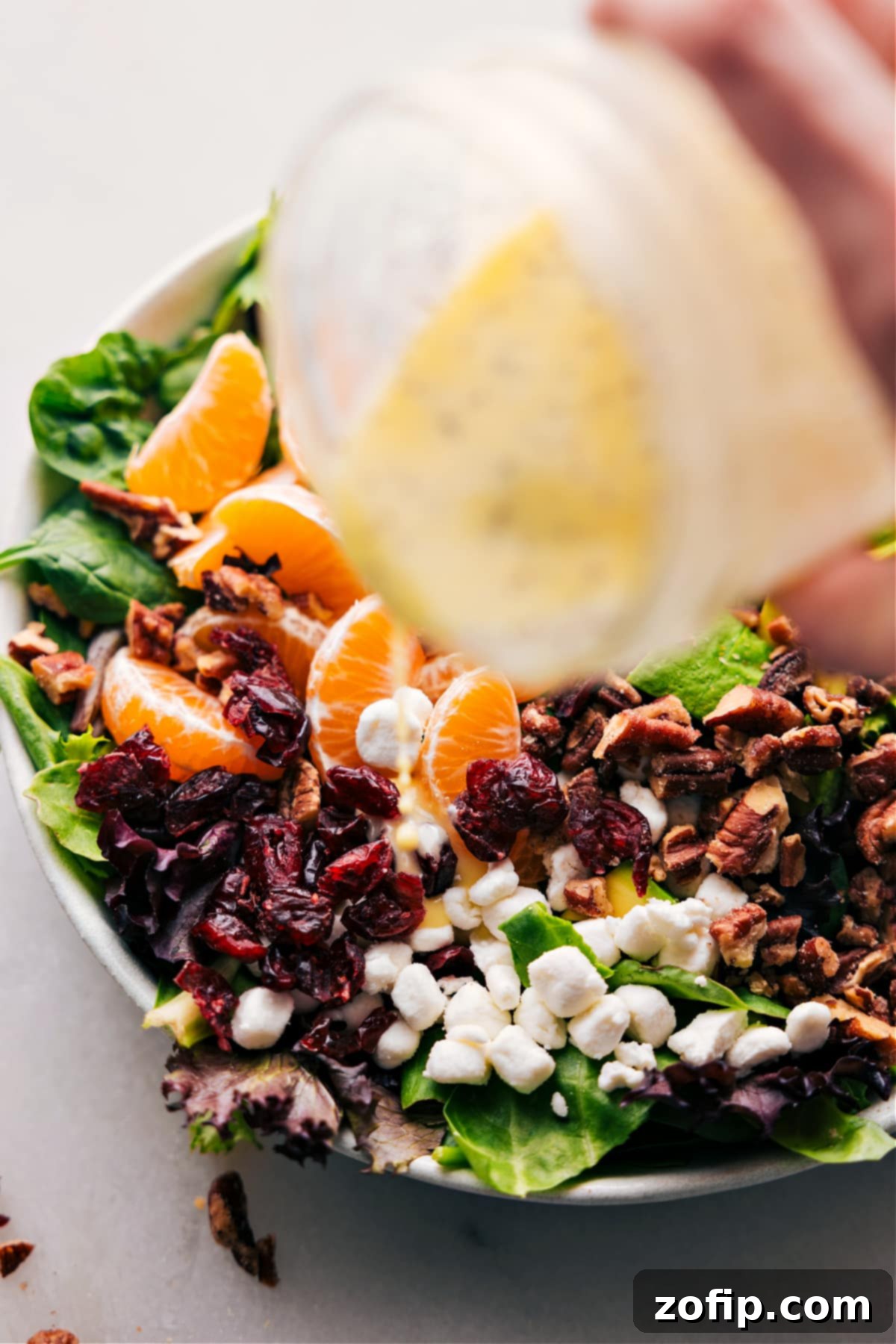 Lemon poppy seed dressing being poured generously over a vibrant green salad, showcasing its creamy texture.