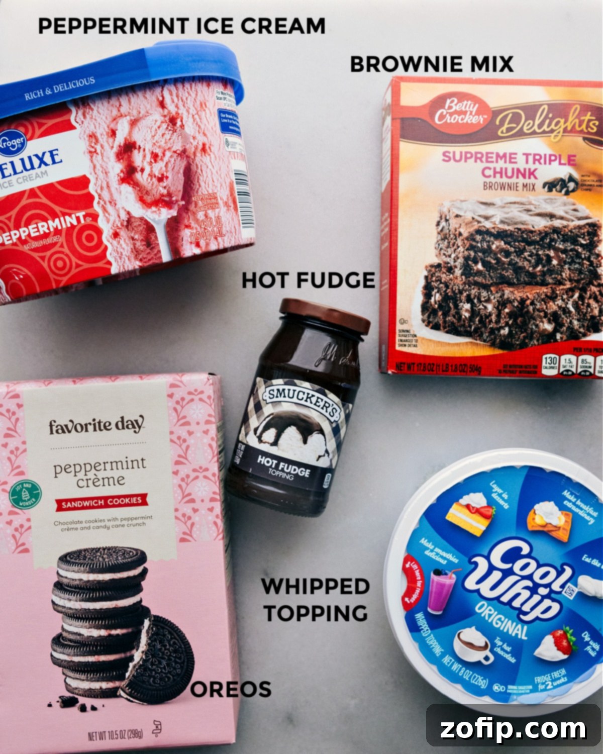 The five essential ingredients for Peppermint Brownie Ice Cream Bars laid out: a box of brownie mix, a package of Oreo cookies, a jar of hot fudge, a tub of peppermint ice cream, and a container of frozen whipped topping. Each ingredient is clearly visible and ready for preparation.