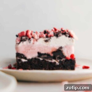A slice of peppermint brownie ice cream bar, displaying its stunning layers with a rich brownie base, a thick layer of ice cream, and a topping of crushed peppermint, exemplifying a perfect blend of textures and flavors.