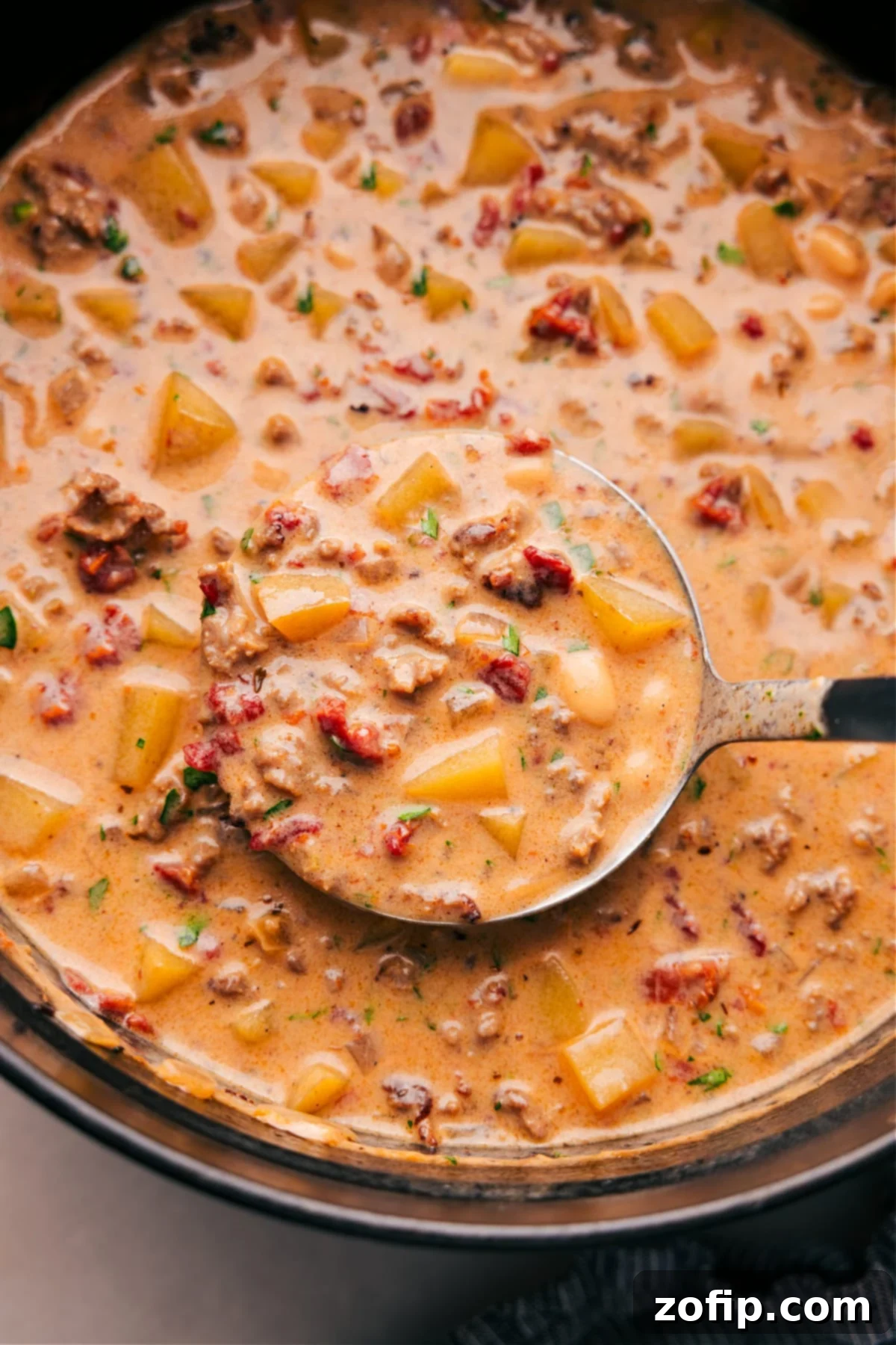 A large pan brimming with the finished Tuscan Sausage and Potato Soup, rich with visible pieces of sausage, diced potatoes, and sun-dried tomatoes, ready to be served as a comforting meal.