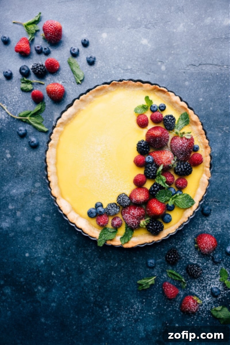 The ultimate homemade Lemon Tart: A buttery crust cradling a tangy, creamy lemon filling, beautifully finished with fresh berries and a dusting of powdered sugar. Perfect for any occasion! #lemontart #betterthanpie #custard #tartsweet #lemony #dessertrecipe Overhead view of a perfectly baked Lemon Tart garnished with fresh berries and powdered sugar, ready to be served.