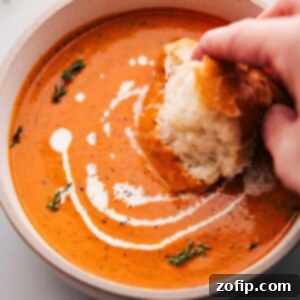 Smoky Red Pepper Bisque 3 A big bowl of vibrant Roasted Red Pepper Soup being served, with a piece of crusty bread dipped in, highlighting its creamy texture.