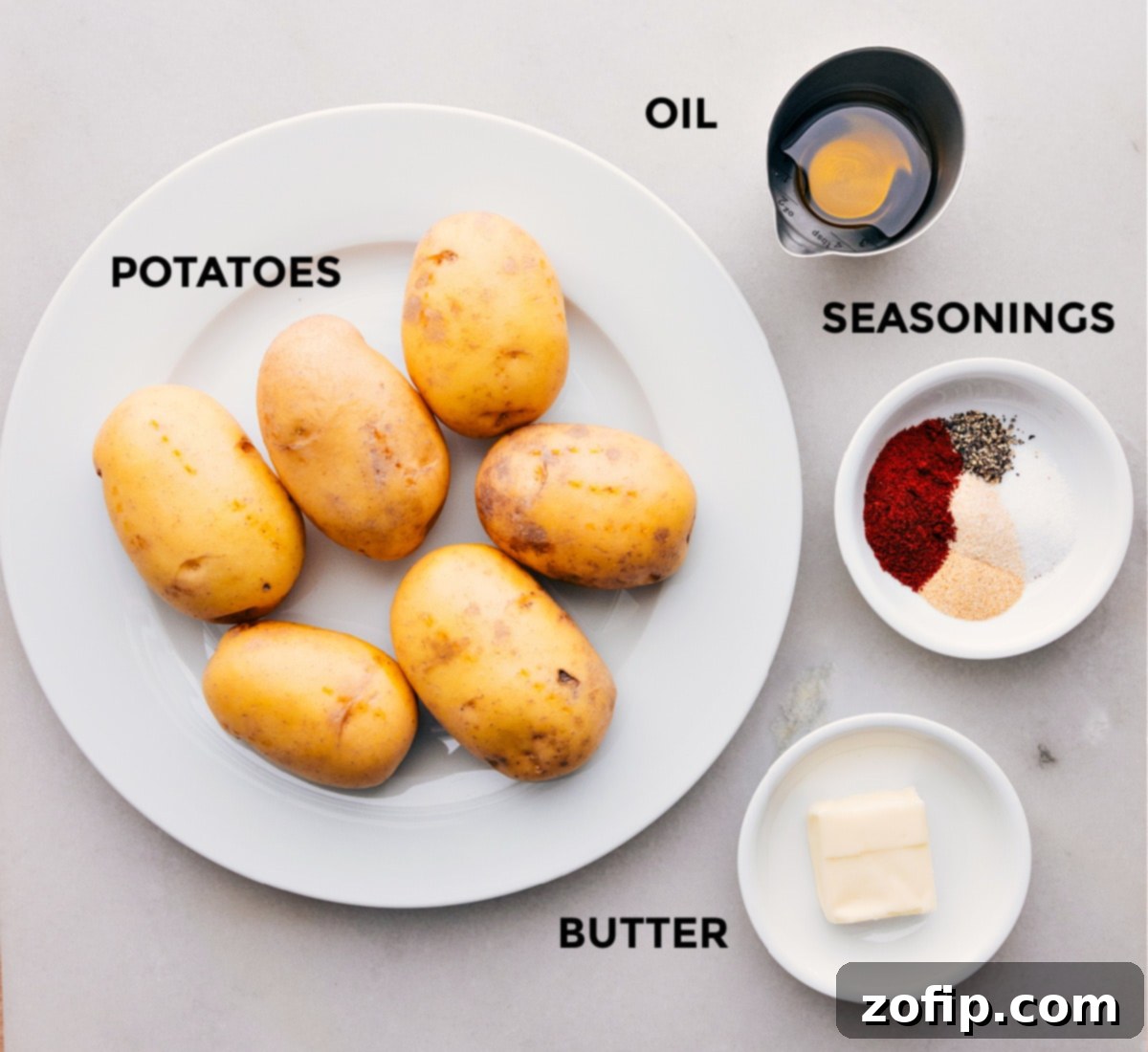 All fresh ingredients for skillet breakfast potatoes laid out on a wooden board, including golden potatoes, butter, olive oil, and various spices.