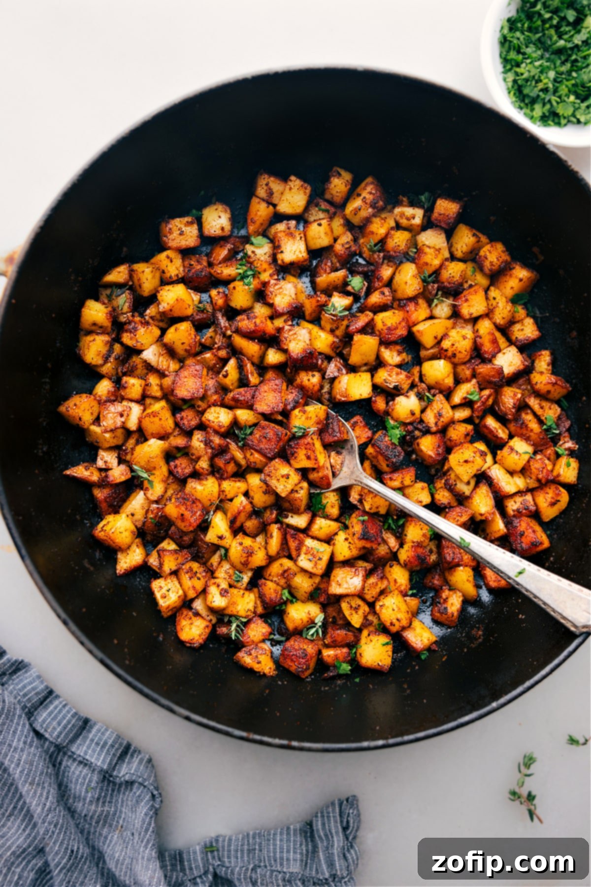 A close-up of a plate piled high with golden-brown, freshly cooked Skillet Breakfast Potatoes, garnished with fresh herbs, ready to be enjoyed.