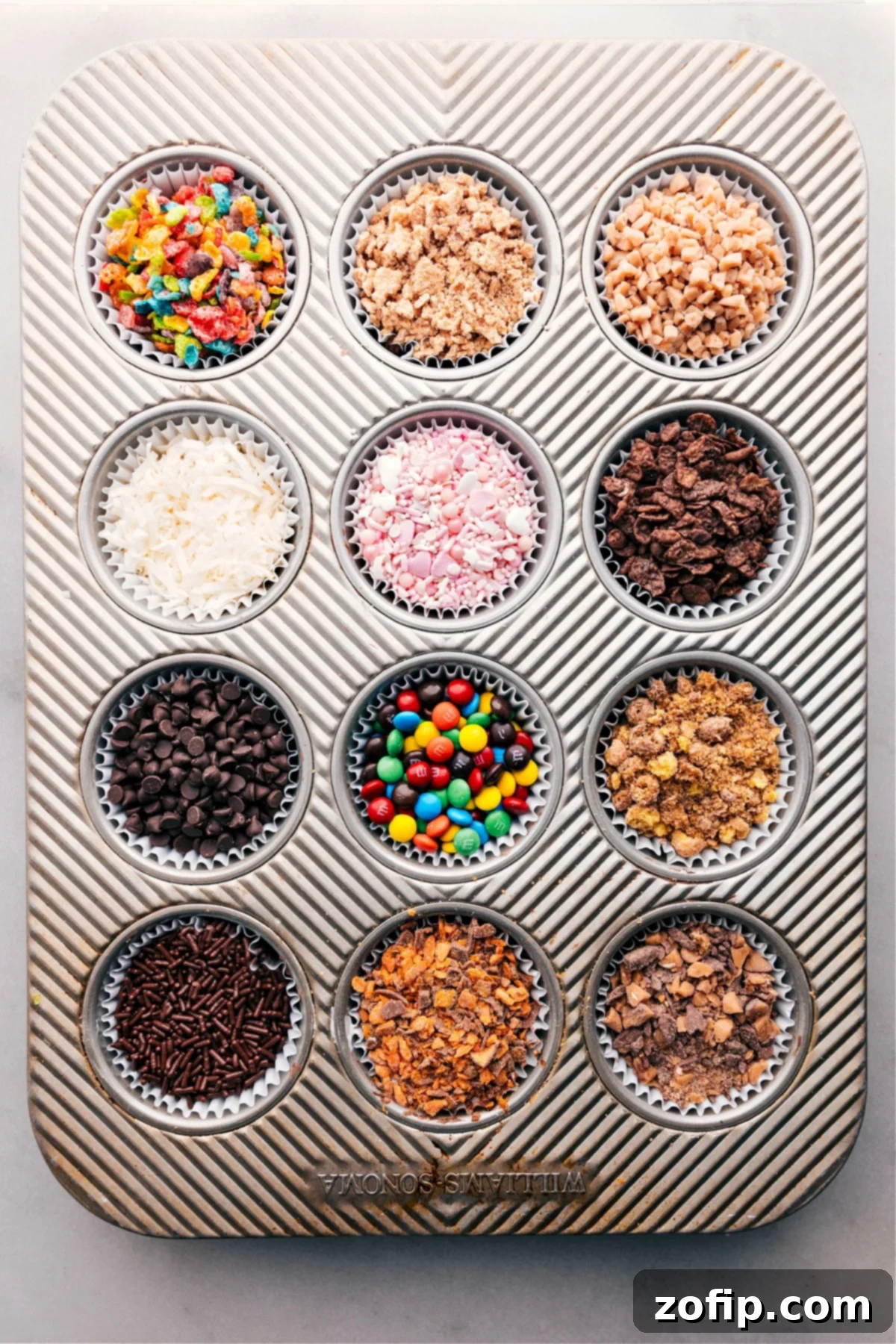 An Assortment of Toppings for Your Dessert Bar. An overhead shot of a muffin pan, each well filled with a different colorful topping like crushed cookies, sprinkles, and nuts, ready for a chocolate-covered strawberry bar.