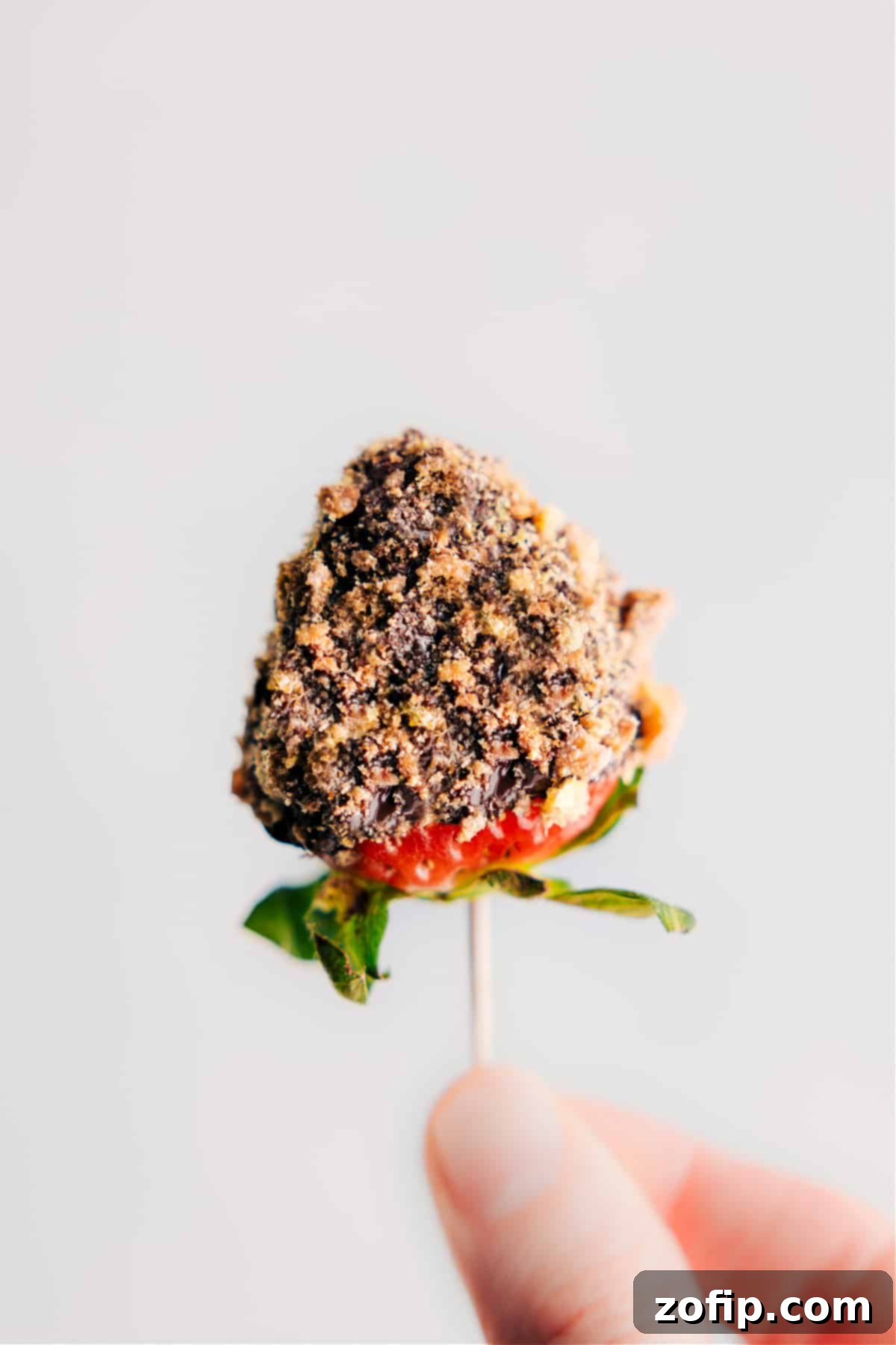 Delicious Chocolate Dipped Strawberry with Cookie Crumbs. A perfectly dipped strawberry covered in smooth chocolate, generously sprinkled with cookie crumbs, placed on parchment paper ready to set.