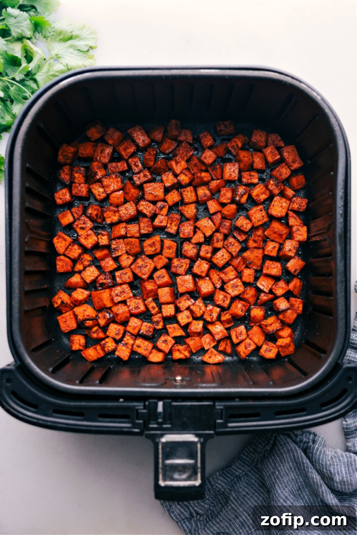 Photo looking down at an air fryer with perfectly cooked sweet potato cubes in the basket, fresh out of the air fryer.