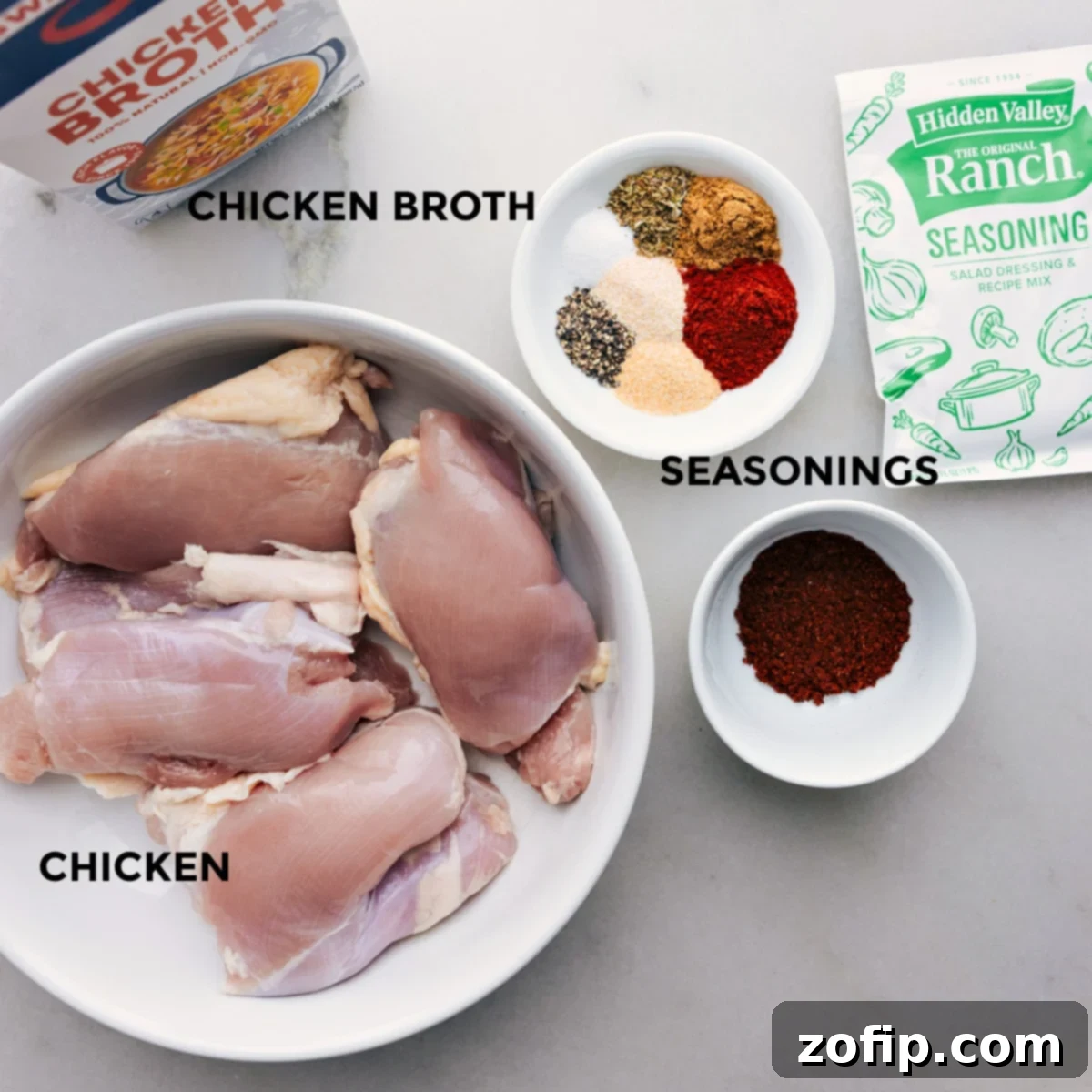 Ingredients for Crockpot Chicken Tacos laid out on a counter, including chicken thighs, seasoning packets, and broth.