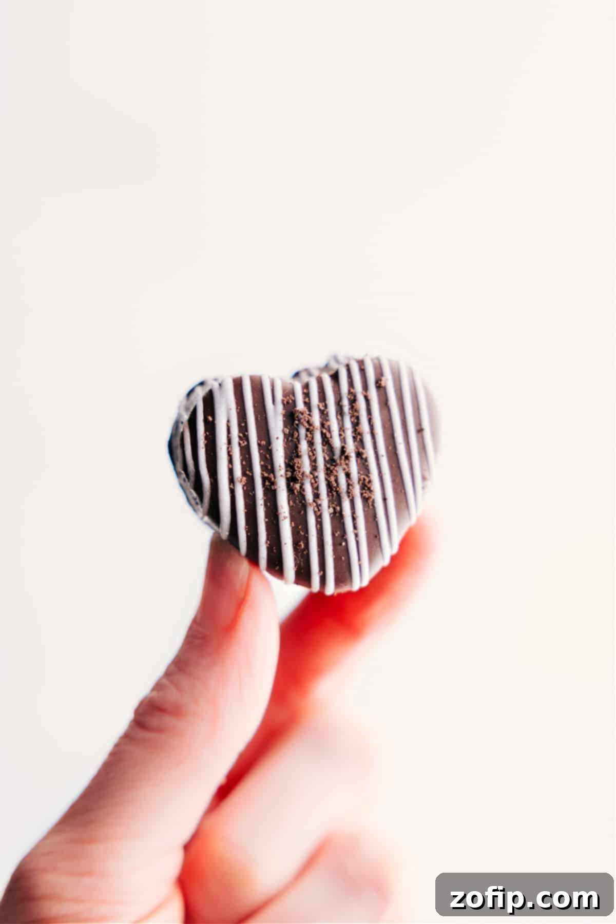 A single, perfectly crafted Heart Oreo Truffle held delicately, showcasing its rich chocolate coating and appealing shape.