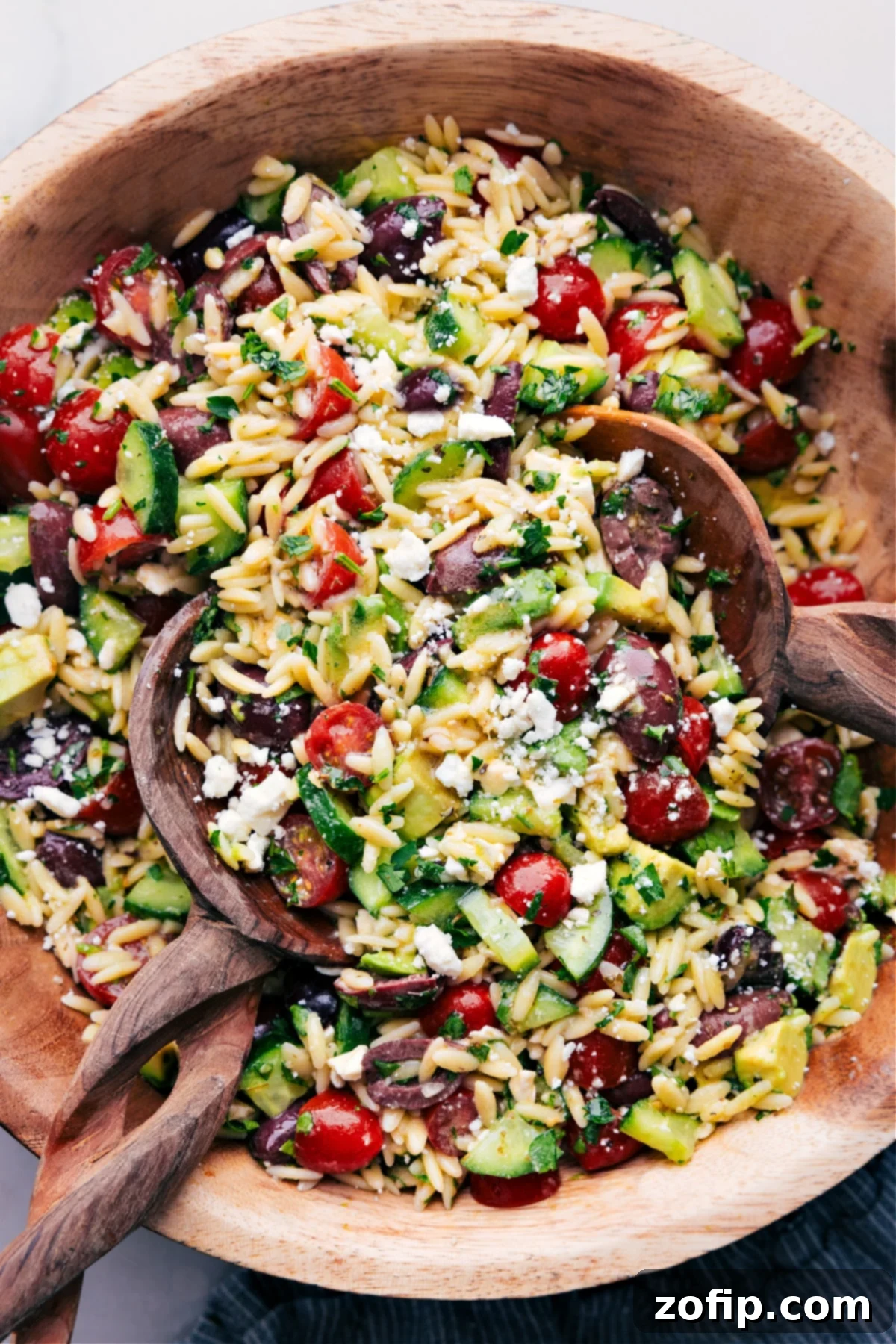 Wooden spoons, tossing a batch of Mediterranean Orzo Salad, showcasing its vibrant colors and fresh ingredients.
