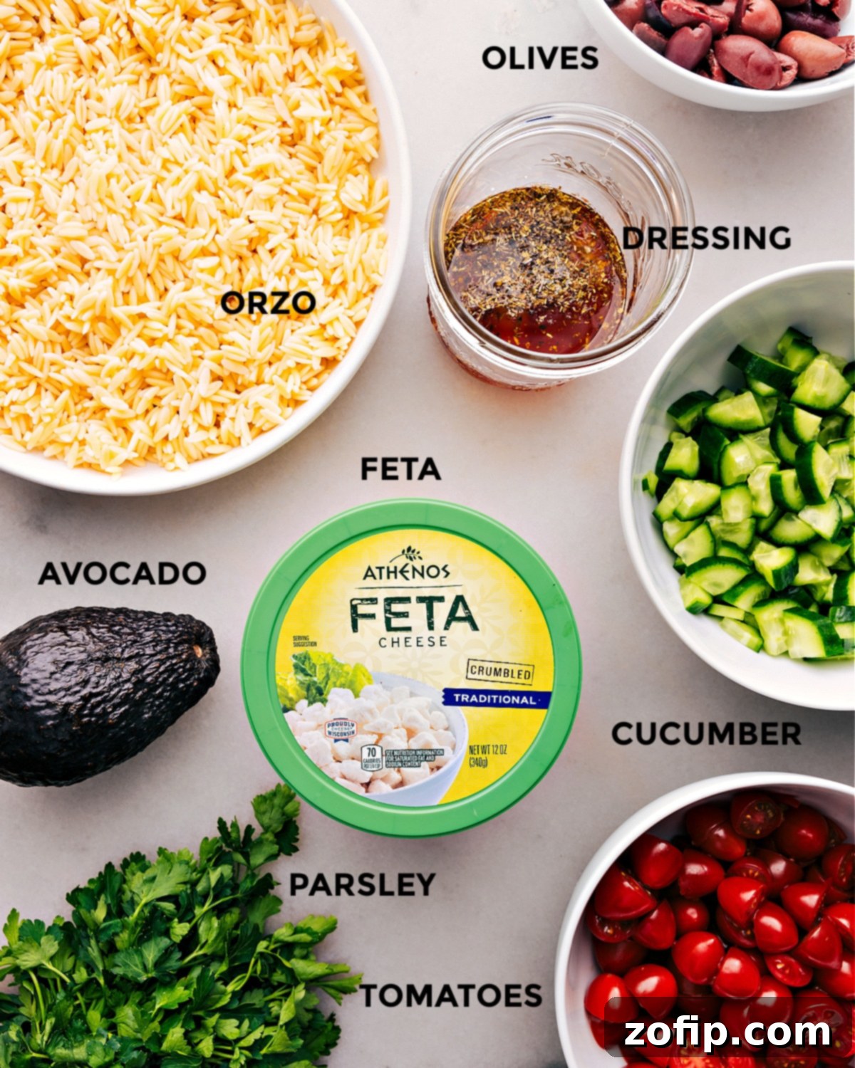 All the fresh ingredients used in this Mediterranean Orzo Salad recipe, neatly prepped and arranged for easy preparation, including orzo, tomatoes, cucumbers, olives, feta, avocado, and parsley.