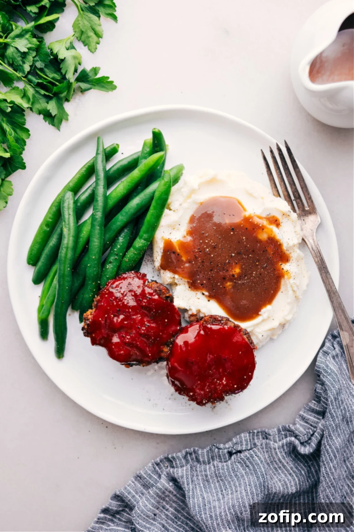 Two perfectly glazed Mini Meatloaves served on a plate with creamy mashed potatoes and vibrant green beans, ready to be enjoyed.