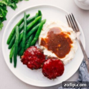 A delicious Mini Meatloaf on a plate, perfectly glazed and served alongside fluffy mashed potatoes and crisp green beans.
