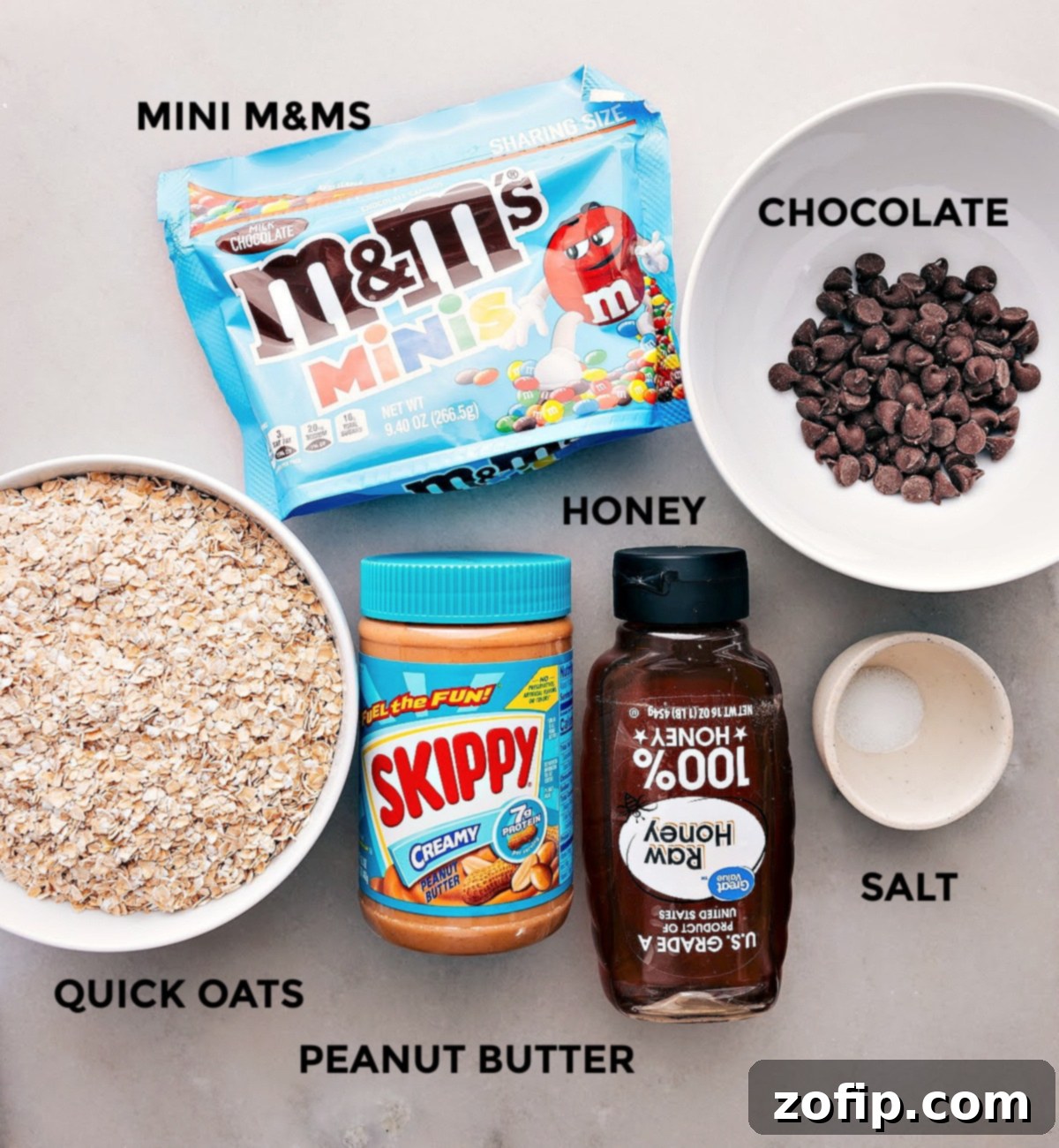 All the core ingredients for the energy bars recipe, including quick oats, peanut butter, honey, salt, and miniature M&Ms, neatly prepped and ready for assembly.