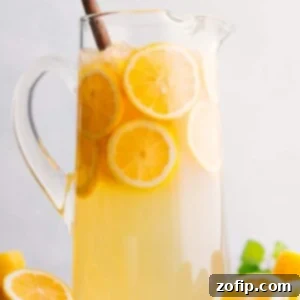A glass of homemade lemonade garnished with a lemon slice and a sprig of mint, next to a pitcher filled with more lemonade.