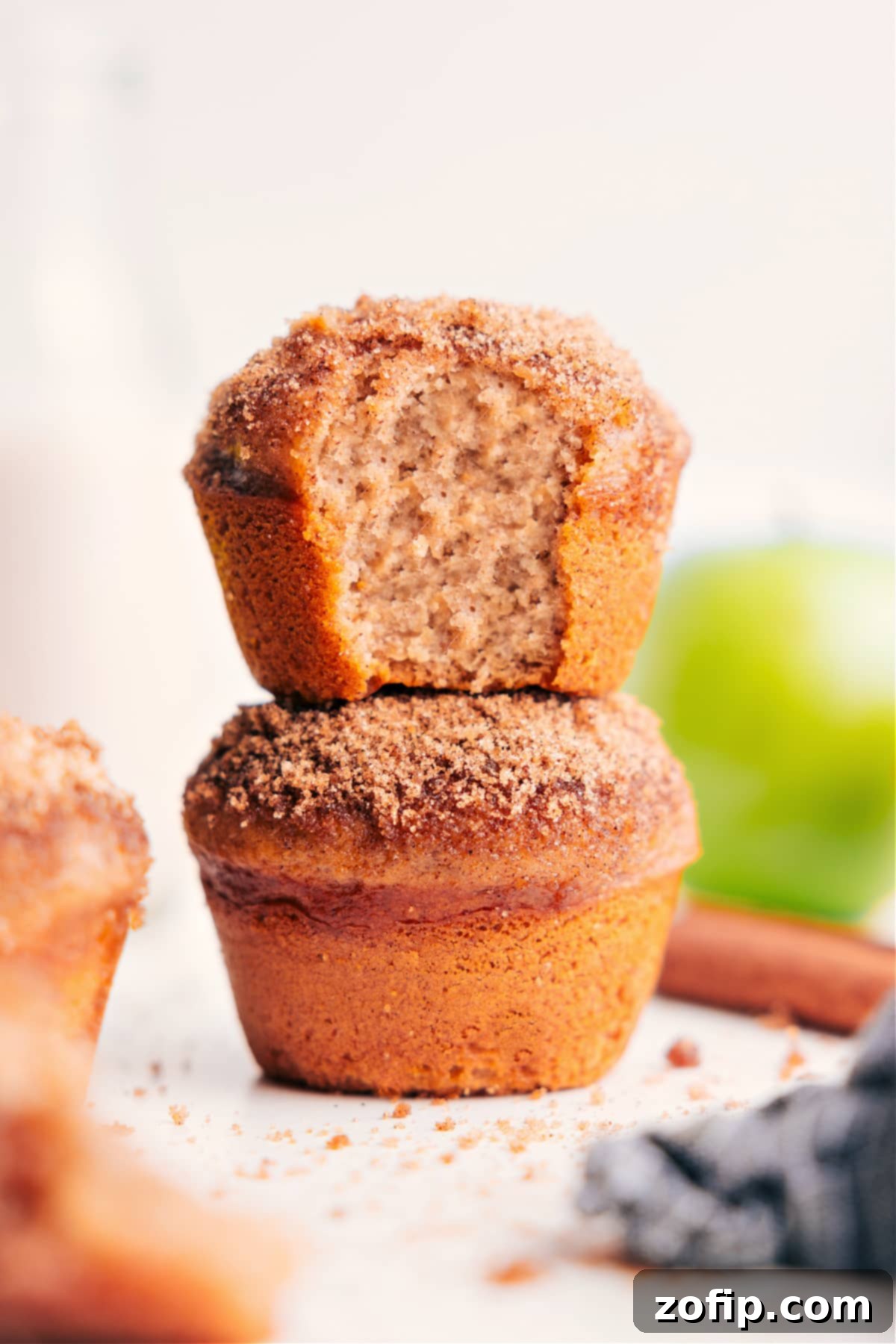 Two freshly baked applesauce muffins with a golden-brown cinnamon-sugar topping, stacked appealingly on a white plate with a rustic wooden background.