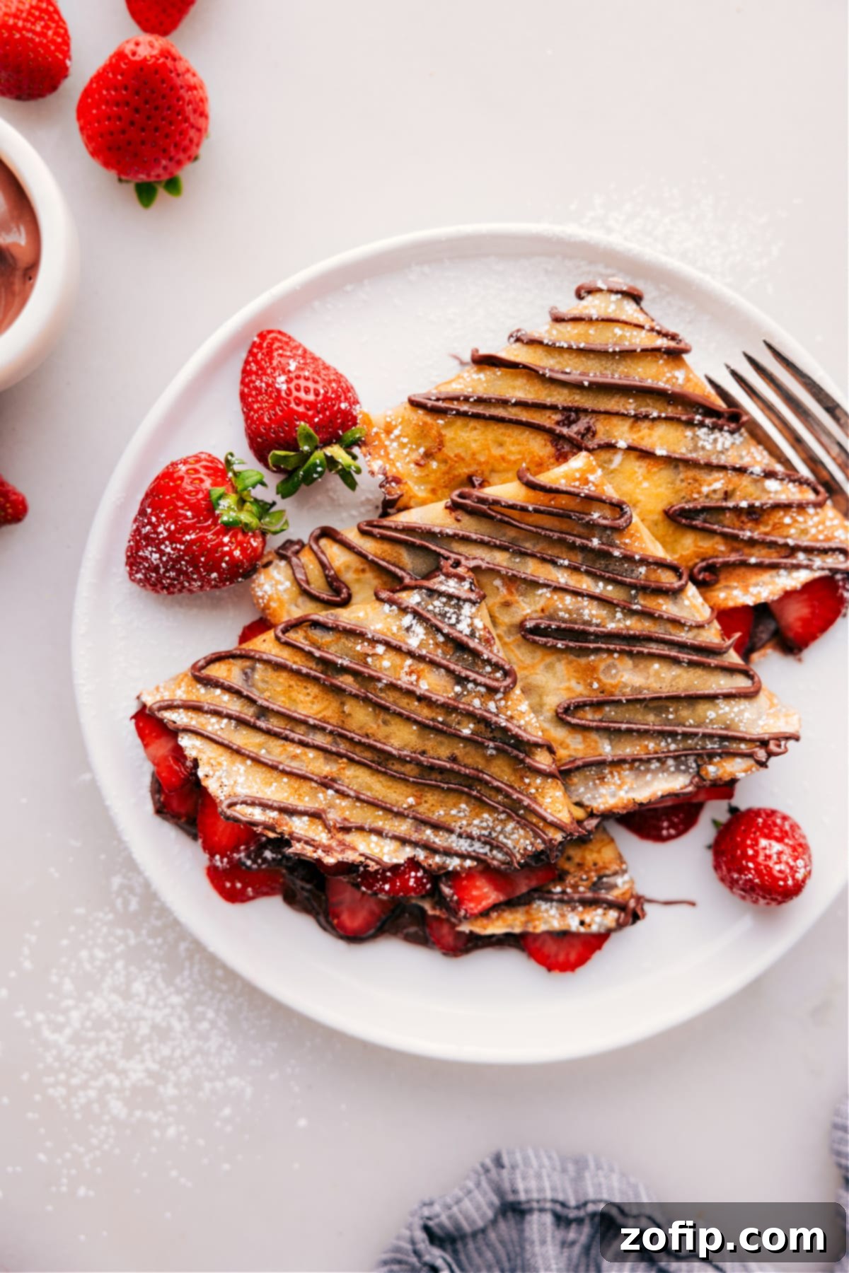 Finished Nutella crepes, generously filled with strawberries and cream, with a rich Nutella drizzle on top and a dusting of powdered sugar.