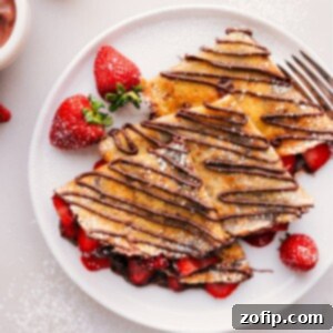 Finished Nutella crepes, generously filled with strawberries and cream, with a rich Nutella drizzle on top and a dusting of powdered sugar.