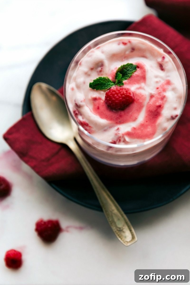 A close-up, overhead view of the vibrant pink Raspberry Fluff, beautifully set and garnished with a few fresh raspberries, elegantly presented in a glass bowl, ready to be enjoyed.